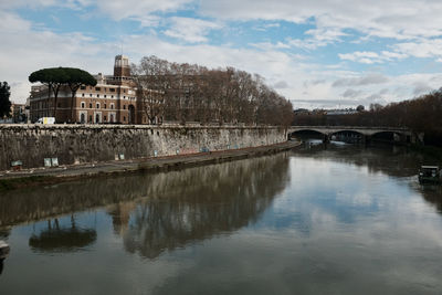 Arch bridge over river by buildings against sky