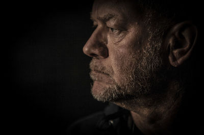 Close-up of man looking away while standing against black background