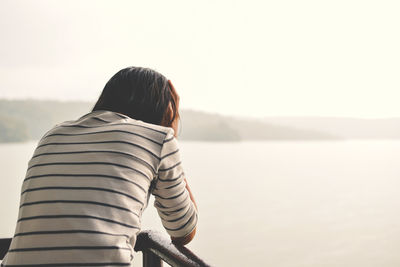 Rear view of woman leaning on railing during foggy weather