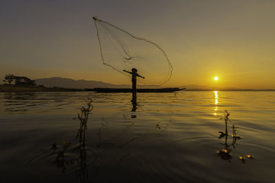 Silhouette fishing net in lake against sky during sunset
