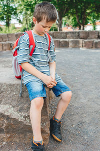 A sad schoolboy sits in the school yard with a backpack on his back. children's problems at school.