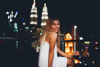 Portrait of smiling young woman in city at night