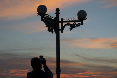 Low angle view of silhouette man standing by old-fashioned lamppost against sky during sunset