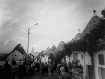 People walking on street amidst buildings in city against sky