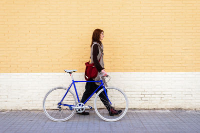 Young smiling woman walking on a city street with bicycle