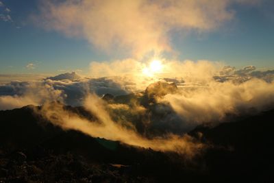 Low angle view of sunlight streaming through clouds during sunset