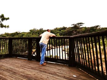 Rear view of man standing on footbridge against clear sky