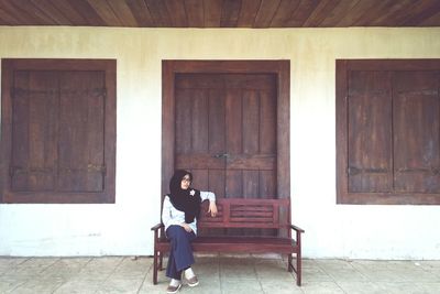 Full length of woman sitting on seat outside building