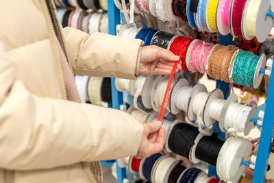 Women's hands choose a red ribbon from multicolored ribbons on a window display in a craft store