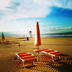 Deck chairs on beach against sky