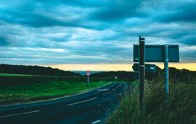 Road sign on field against sky