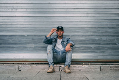 Full length portrait of young man sitting against wall