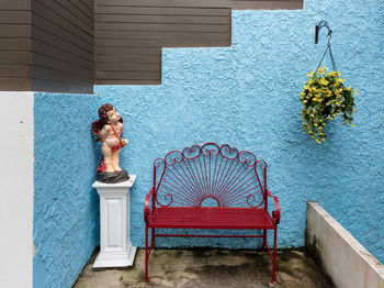 Empty red bench by statue against blue wall at porch
