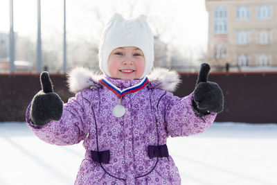 Portrait of smiling girl wearing warm clothing while showing thumbs up outdoor