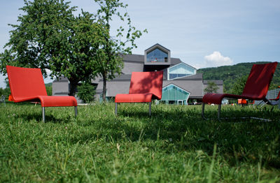 Empty chairs on field by swimming pool against sky