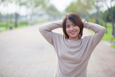 Close-up portrait of young woman with hands behind head standing outdoors