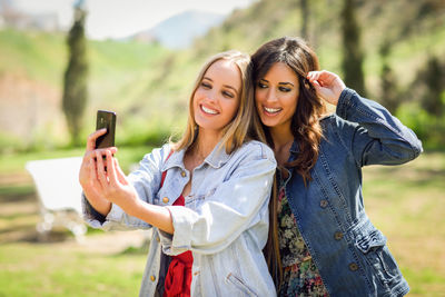 Smiling young woman taking selfie with friend from mobile phone on field