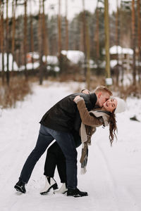 A happy couple in love in winter clothes hugging together walking in a snowy forest on an weekend