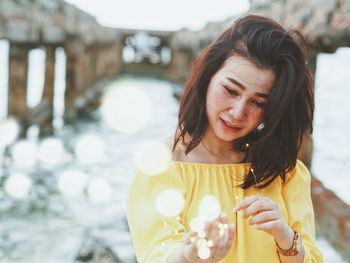 Woman holding illuminated string lights while standing outdoors