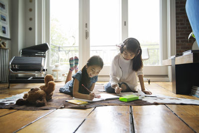 Sisters writing in book on carpet at home