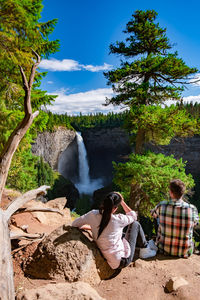 People sitting on rocks by plants against sky