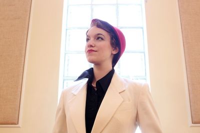 Low angle view of young woman looking away while standing against window