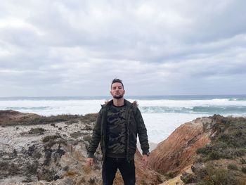 Portrait of young man standing on rock by sea against sky