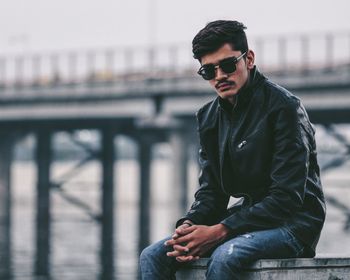 Fashionable man wearing sunglasses sitting against bridge