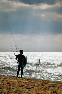 Rear view of windsurfer standing at beach against sky