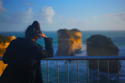 Rear view of woman photographing by sea against sky