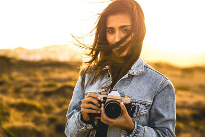 Portrait of young woman photographing against sky during sunset