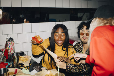 Waitress pointing while woman with burger ordering food by friend in cafe