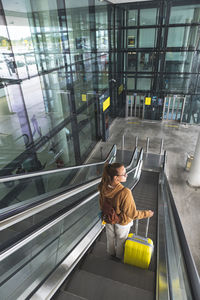 Young woman with luggage standing on escalator