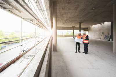 Two men with plan wearing safety vests talking in building under construction