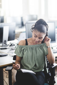 Confident teenage girl learning from book while sitting on chair in computer lab at high school