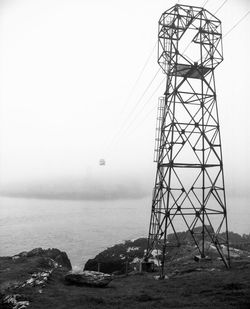 Electricity pylon by sea against clear sky