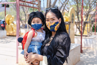 Little child girl and asian mother wearing medical protective mask and holding her daughter 