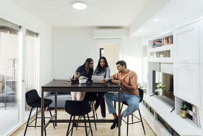 Young woman sharing tablet pc with man and woman at table in living room