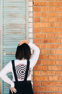 Rear view of woman standing against brick wall