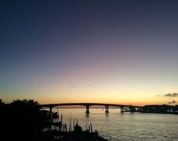 Silhouette bridge over river against sky during sunset