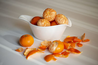 Peeling tangerines or clementines in white dish, isolated on white background