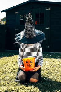 Halloween concept. a girl in a witch costume and a hat that covers her face sits on the grass 