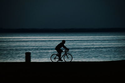 Silhouette of man cycling on shore at night