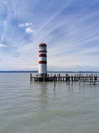 Lighthouse on sea by building against sky