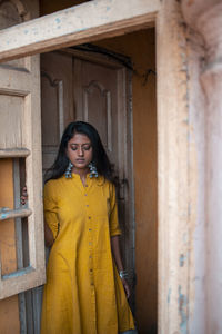 Portrait of woman standing against yellow wall