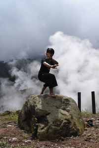 Young man practicing karate on rock formation in foggy weather