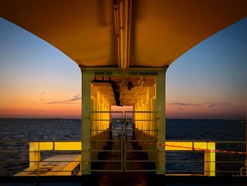 Empty bridge over sea against sky during sunset