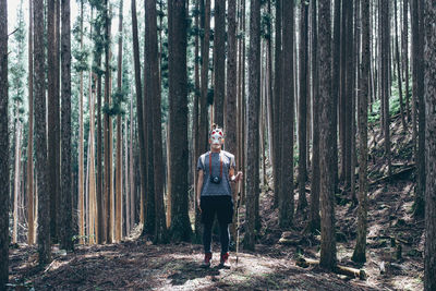 Portrait of young woman standing amidst trees in forest