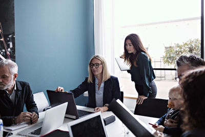 Businesswomen discussing over laptops with colleagues working at conference table in board room