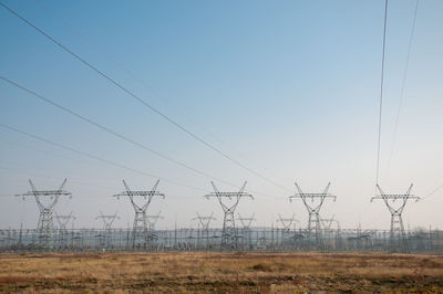 Electricity pylons on field against clear sky